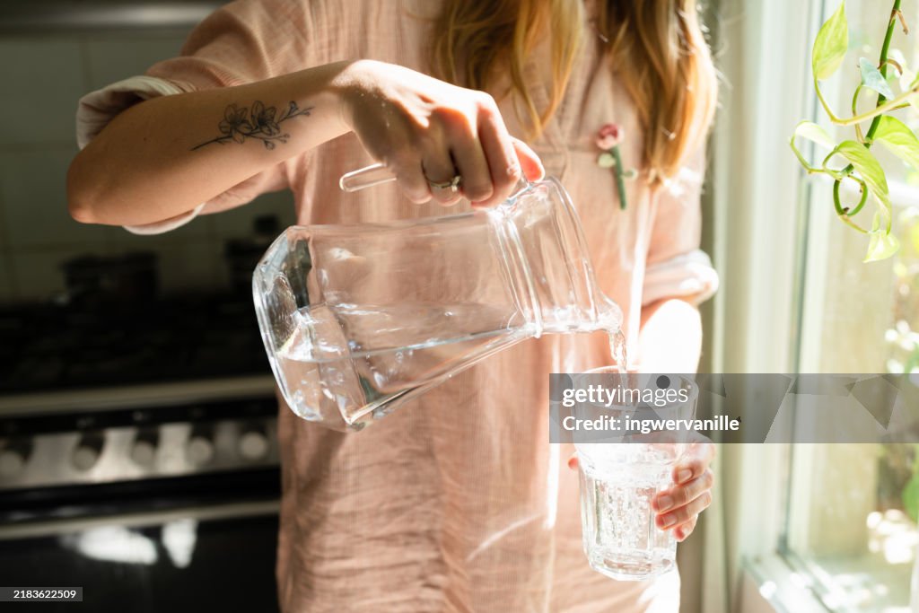 Woman pouring water in a glass from a jug in the kitchen
