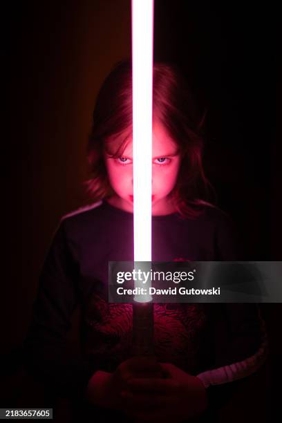 a menacing little girl with expressive eyes holding a red light saber before her face on black background - laser sword stock pictures, royalty-free photos & images