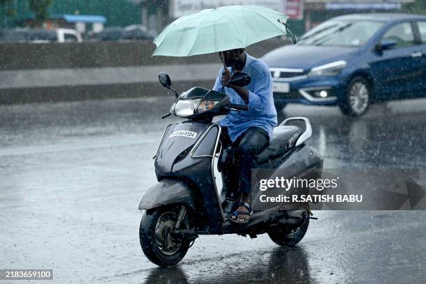 Man holds an umbrella whilst riding his motorbike along a street amid rainfall in Chennai on November 12, 2024.