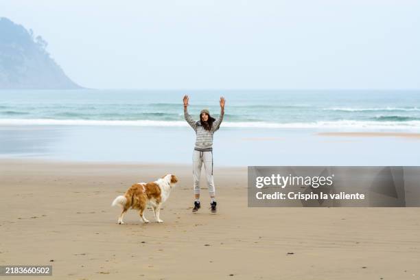 a woman exercises on the beach, her dog watches playfully - vorruhestand stock-fotos und bilder