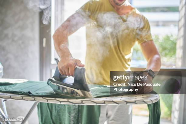 man ironing laundry on a board at home - stirare foto e immagini stock