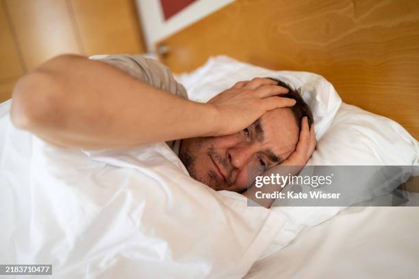 mature man suffering from pain and laying in bed covered with blanket. melancholy mood, mental health. life problem - negative emotion stock pictures, royalty-free photos & images