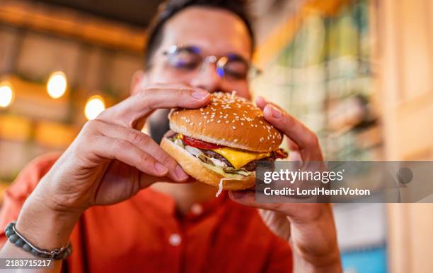 young man eating a tasty burger - snabbmat bildbanksfoton och bilder