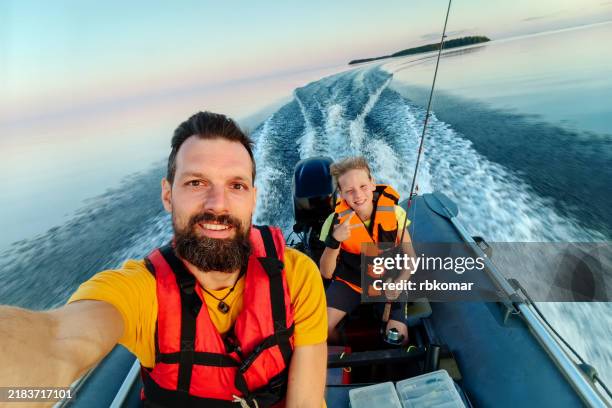 father and son enjoying a high-speed boat ride at sunset on a calm lake - outboard motor stock pictures, royalty-free photos & images