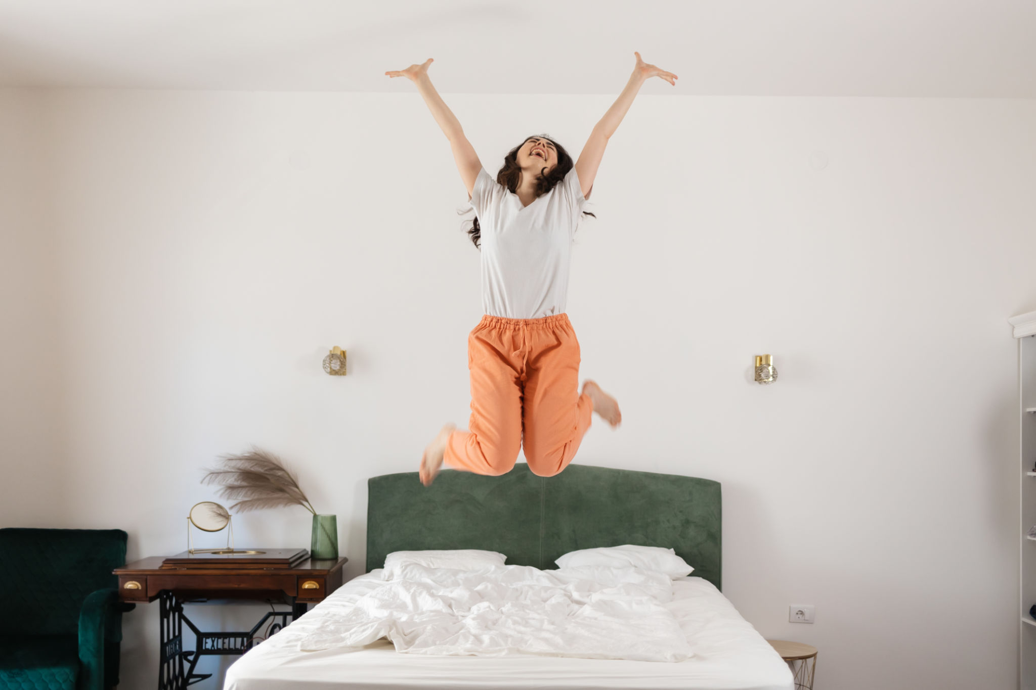 Happy young Caucasian woman dances and jumps on bed in bedroom. Enjoying winning. Freedom and relax at home Happy young Caucasian woman dances and jumps on bed in bedroom. Enjoying winning. Freedom and relax at home