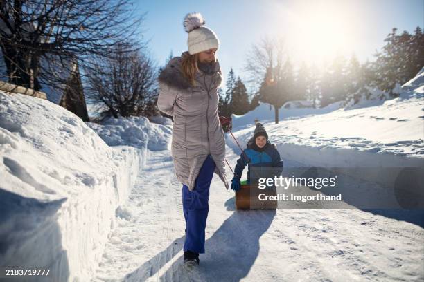 mother pulling son on toboggan on a sunny winter day - sledding stock pictures, royalty-free photos & images