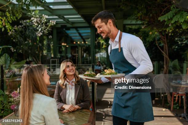 waiter serving food to two business woman at a cafe outdoors - ober stockfoto's en -beelden