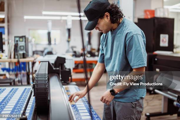 male worker operating large format printer and paper cutter in factory - tryckeri bildbanksfoton och bilder
