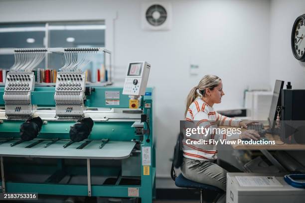 female worker using computer while operating embroidery machine - textielindustrie stockfoto's en -beelden
