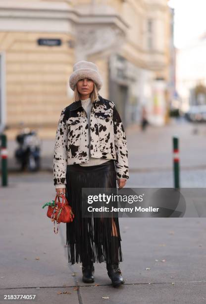 Karin Teigl is seen wearing a cream-white fluffy fake fur hat from Zara, a jacket with cow print, collar and large chest pockets from Mango;...