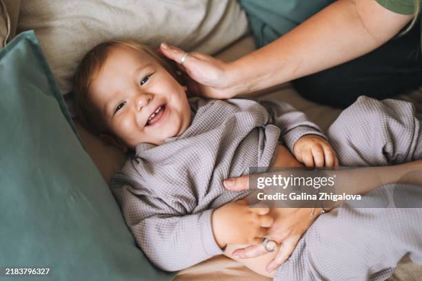 young mother with 11-12 month smiling baby boy lying on beige blanket at home - männliches baby stock-fotos und bilder