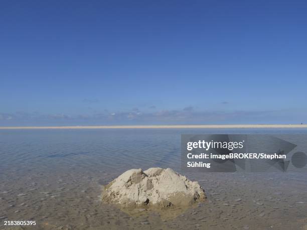 quiet beach with a collection of sand in the foreground and blue sky, wide sky on a lonely north sea beach with a bright blue sky, spiekeroog, germany, europe - ostfriesland stock-fotos und bilder