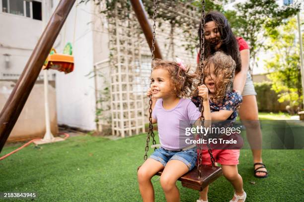 mother playing with her daughters at playground - swinging stock pictures, royalty-free photos & images