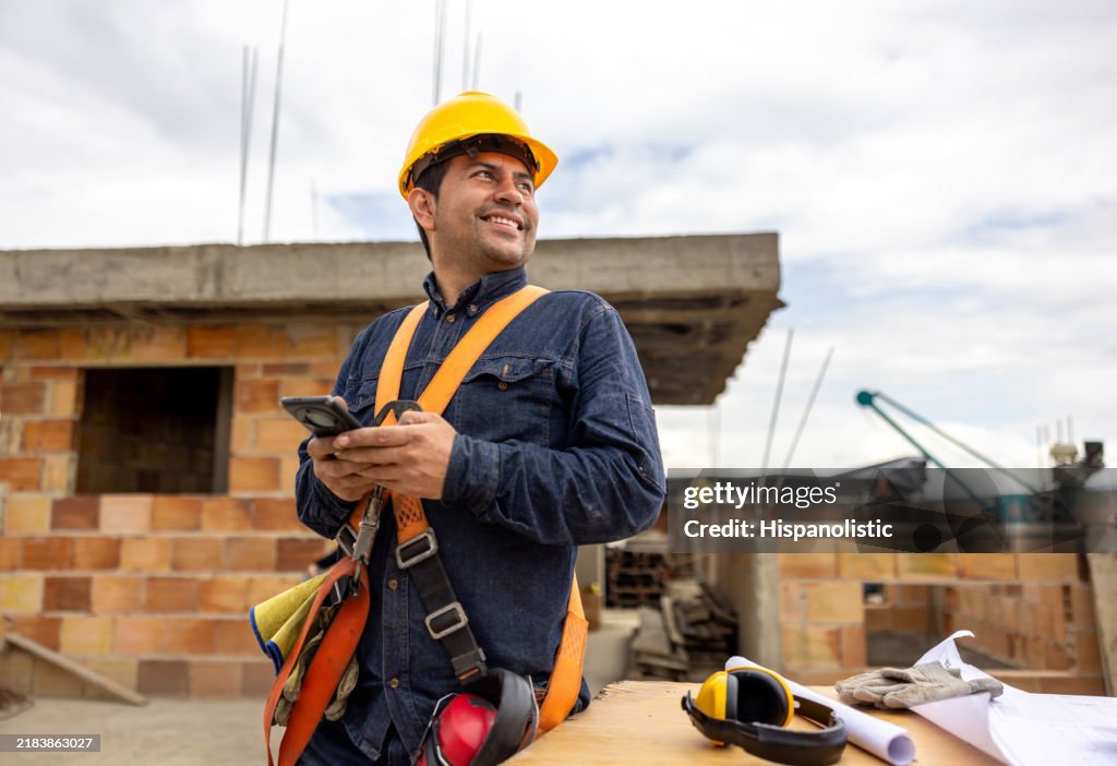 Construction worker smiling and using his cell phone at a building site