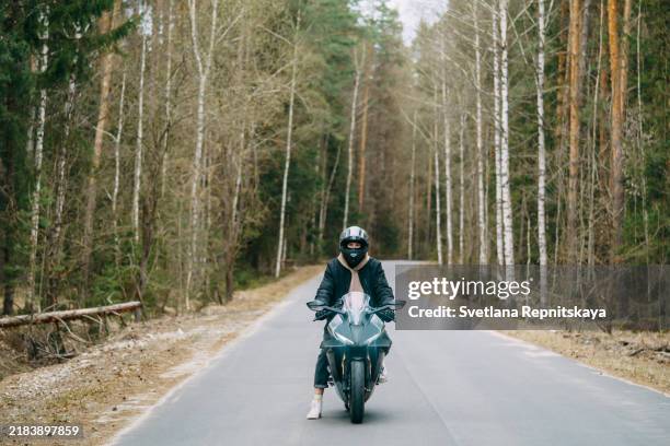 biker rides a motorcycle wearing a helmet surrounded by forest - montare-su-un-veicolo foto e immagini stock