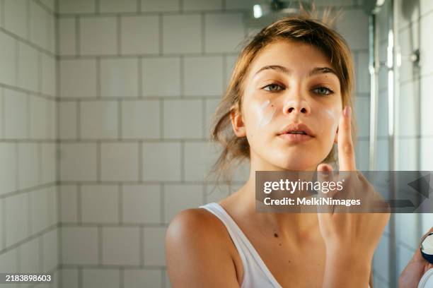 young woman applying hydration creme in the bathroom - gezichtscrème stockfoto's en -beelden