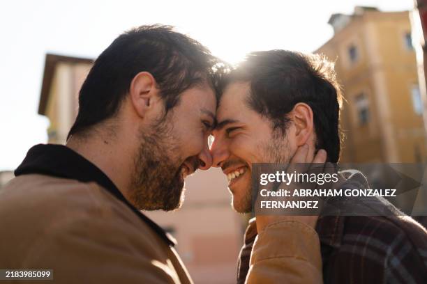 two men in a romantic embrace, touching foreheads and smiling, with cityscape in the background - forehead stock pictures, royalty-free photos & images