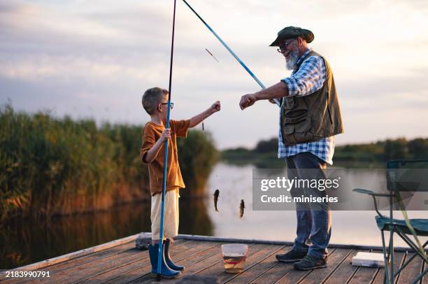 le grand-père et le petit-fils se rapprochent en pêchant au coucher du soleil - industrie de la pêche photos et images de collection