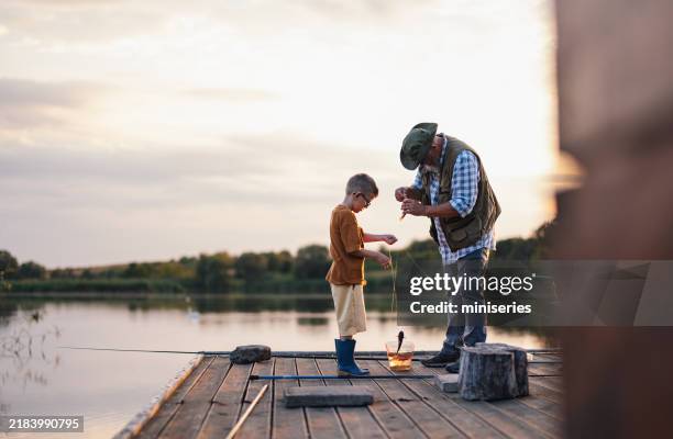 abuelo enseñando a su nieto a pescar en un tranquilo muelle del lago - industria de la pesca fotografías e imágenes de stock