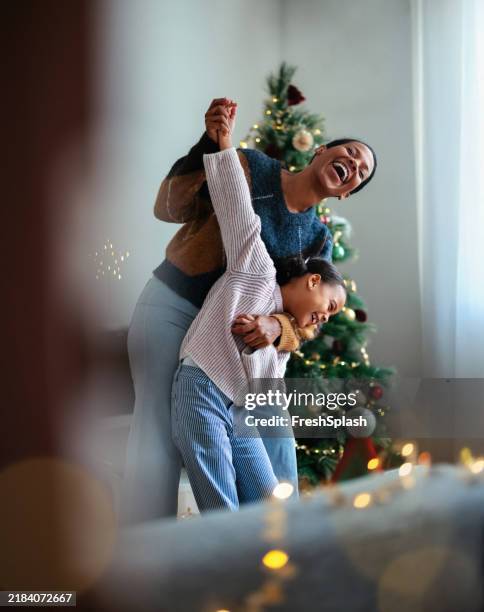 joyful mother and daughter dancing near a christmas tree - hygge stockfoto's en -beelden