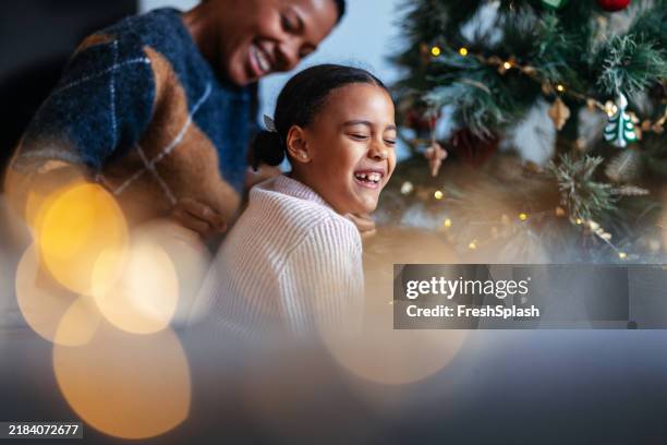 mother and daughter laughing by festive christmas tree - espírito natalino imagens e fotografias de stock