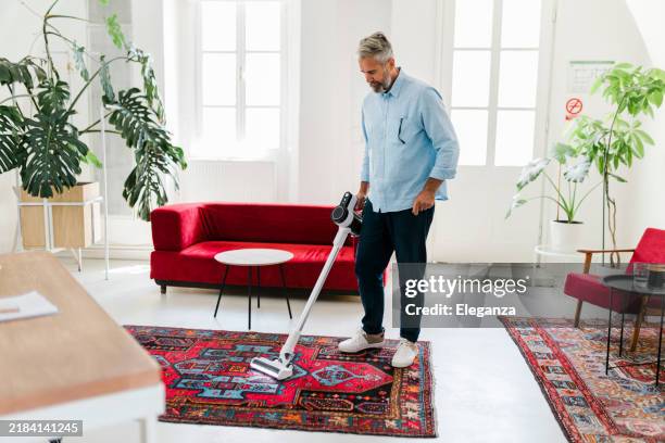 uomo che pulisce la casa con l'aspirapolvere wireless - aspirapolvere foto e immagini stock
