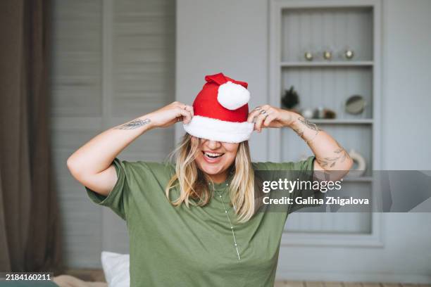 funny young woman plus size in santa hat at home - festieve stemming stockfoto's en -beelden