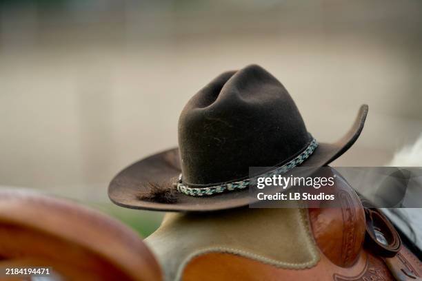 a close-up photo of a brown cowboy hat with a braided hatband resting on a leather saddle - cowboyhut stock-fotos und bilder