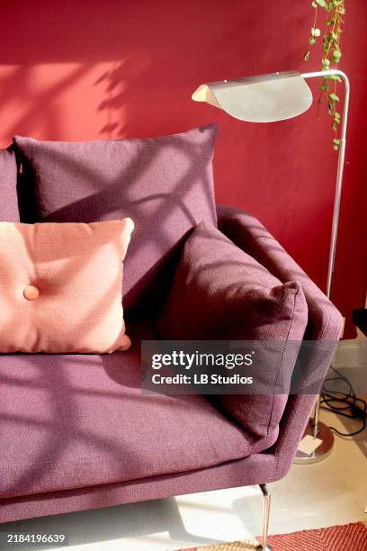 a modern purple armchair with a pink cushion against a vibrant red wall, with plant shadows and a white floor lamp - lámpara de piso fotografías e imágenes de stock