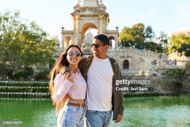 Happy tourists couple walking near fountain in parc de la ciutadella, barcelona, enjoying summer vacation in spain