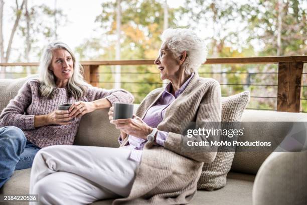 senior mother and daughter having coffee and talking on back porch of vacation home - heißes getränk stock-fotos und bilder