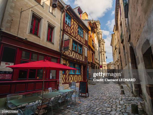 wide angle view of a cobblestone narrow street in the historic district of rennes with traditional multicolour breton stone and half-timbered houses, a cafe terrace and the cathedral, ille-et-vilaine - bretagne (brittany) - western france. - rennes france stock pictures, royalty-free photos & images