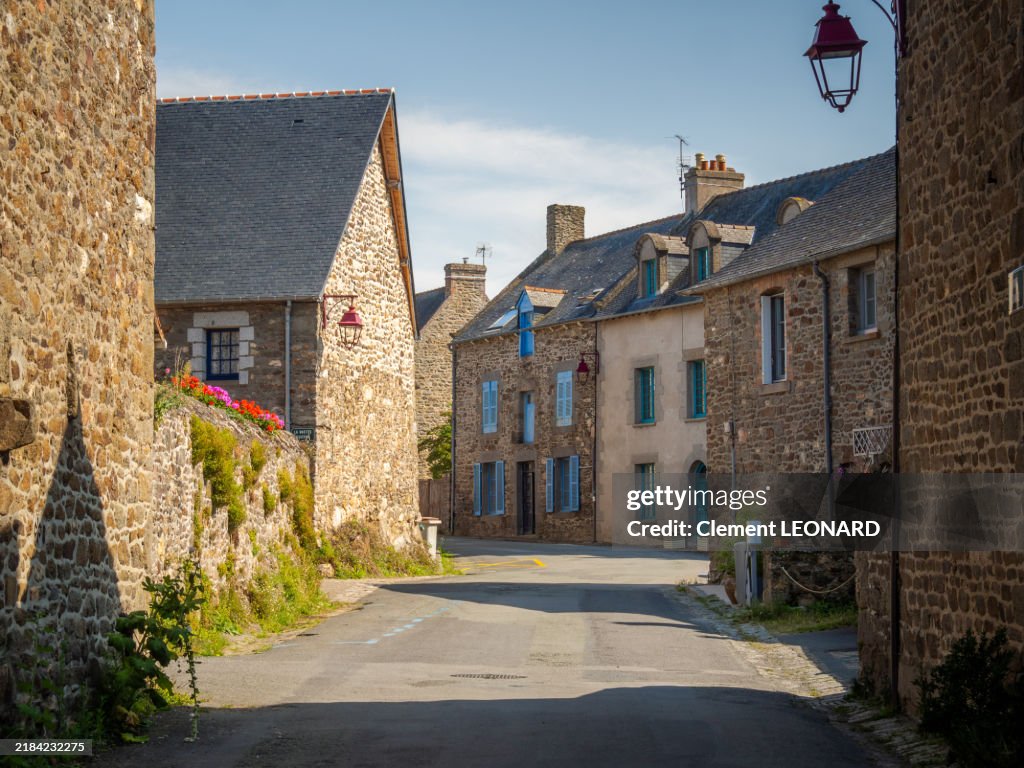 View of a street in the village of Saint-Suliac (Saint Suliac), one of the Plus Beaux Villages de France, with traditional Breton granite houses and their overgrown stone walls decorated with flowers, Ille-et-Vilaine - Bretagne (Brittany) - France.