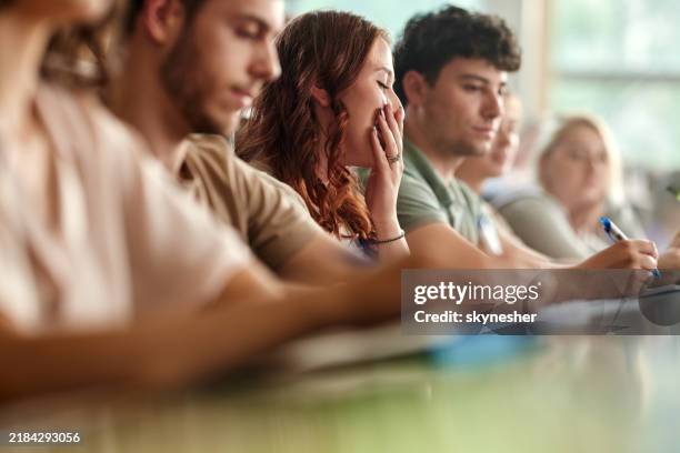 tired female student taking notes on a class in amphitheater. - yawning stock pictures, royalty-free photos & images
