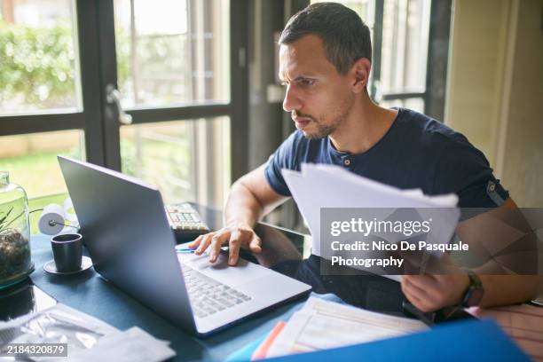 man preparing his taxes at home - formulario de impuestos fotografías e imágenes de stock
