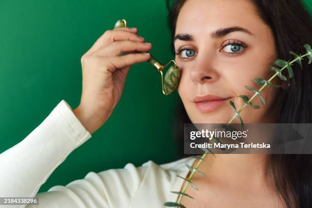 a young woman makes herself a facial massage with a roller. roller for face massage made of natural stone. secrets of youth. - woman cheek stock pictures, royalty-free photos & images