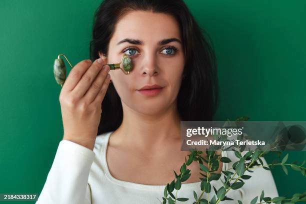 a young woman makes herself a facial massage with a roller. roller for face massage made of natural stone. secrets of youth. - schoonheidsspecialist natuur stockfoto's en -beelden