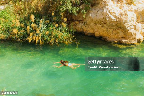 aerial view of woman admiring emerald green river in scenic wadi shab canyon in oman - bimmah sinkhole muscat oman stock pictures, royalty-free photos & images