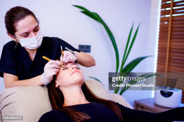une esthéticienne applique des cils artificiels sur une cliente d’un salon de beauté avec des outils de travail dans les mains - maquillage permanent photos et images de collection