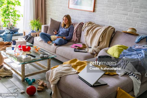 lazy teenager watching tv sitting on the sofa of a messy living room - amontoar imagens e fotografias de stock