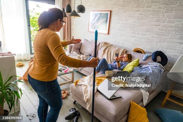 mutter schimpft mit ihrer faulen teenager-tochter in einem unordentlichen wohnzimmer - regeln stock-fotos und bilder