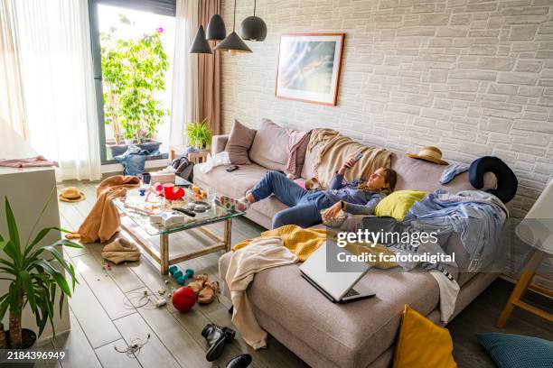 lazy teenager girl using phone on the sofa of a messy living room - lättja bildbanksfoton och bilder
