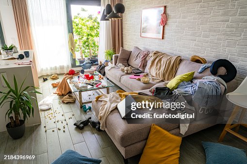 Upset woman head in hands contempling her messy and dirty living room Upset woman head in hands contempling her messy and dirty living room