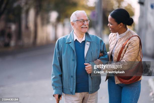 senior man and young woman walking together in the park - two elderly friends chatting in a community park stock pictures, royalty-free photos & images