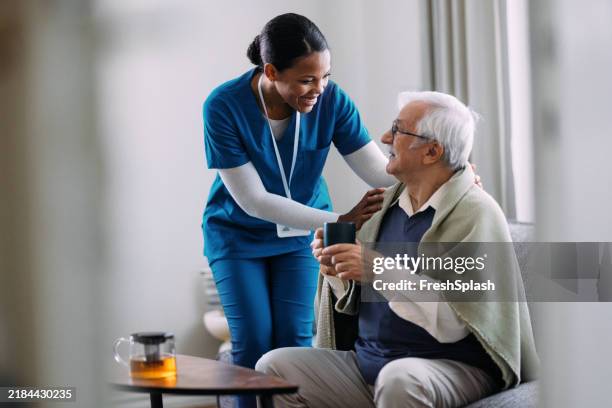 caring nurse assisting elderly man at home with warm smile - patience stock pictures, royalty-free photos & images