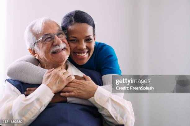caring nurse embracing happy elderly man in warm moment - gezondheidszorg beroep stockfoto's en -beelden