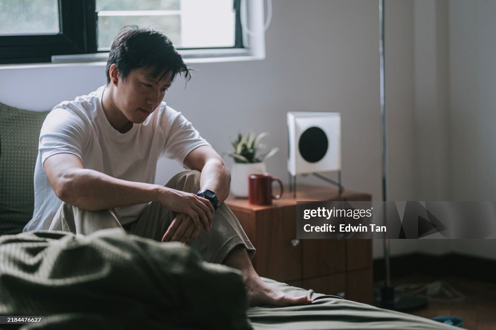 Triste uomo cinese asiatico seduto sul letto