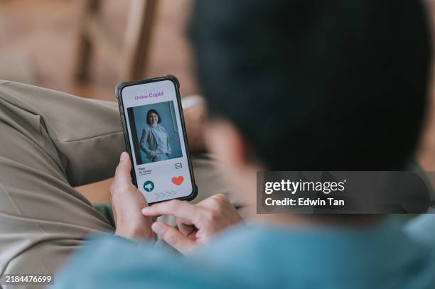 asian man browsing mobile online dating app at home. using an online dating app on smartphone, looking for love on the internet. social media. internet dating. couple relationship. love concept - dating app stock pictures, royalty-free photos & images