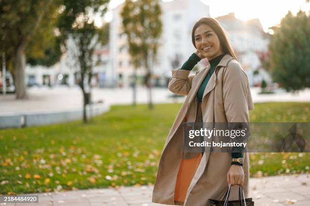 happy woman on the way back from shopping - trenchcoat stockfoto's en -beelden