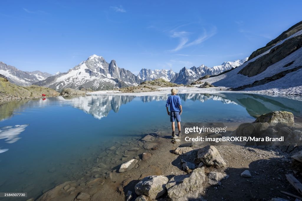 Mountaineer in front of mountain landscape with mountain lake, tourist at Lac Blanc with water reflection, mountain peak Aiguille Verte, Grandes Jorasses, Aiguille du Moine and Mont Blanc, Mont Blanc massif, Chamonix-Mont-Blanc, Haute-Savoie, France, Euro